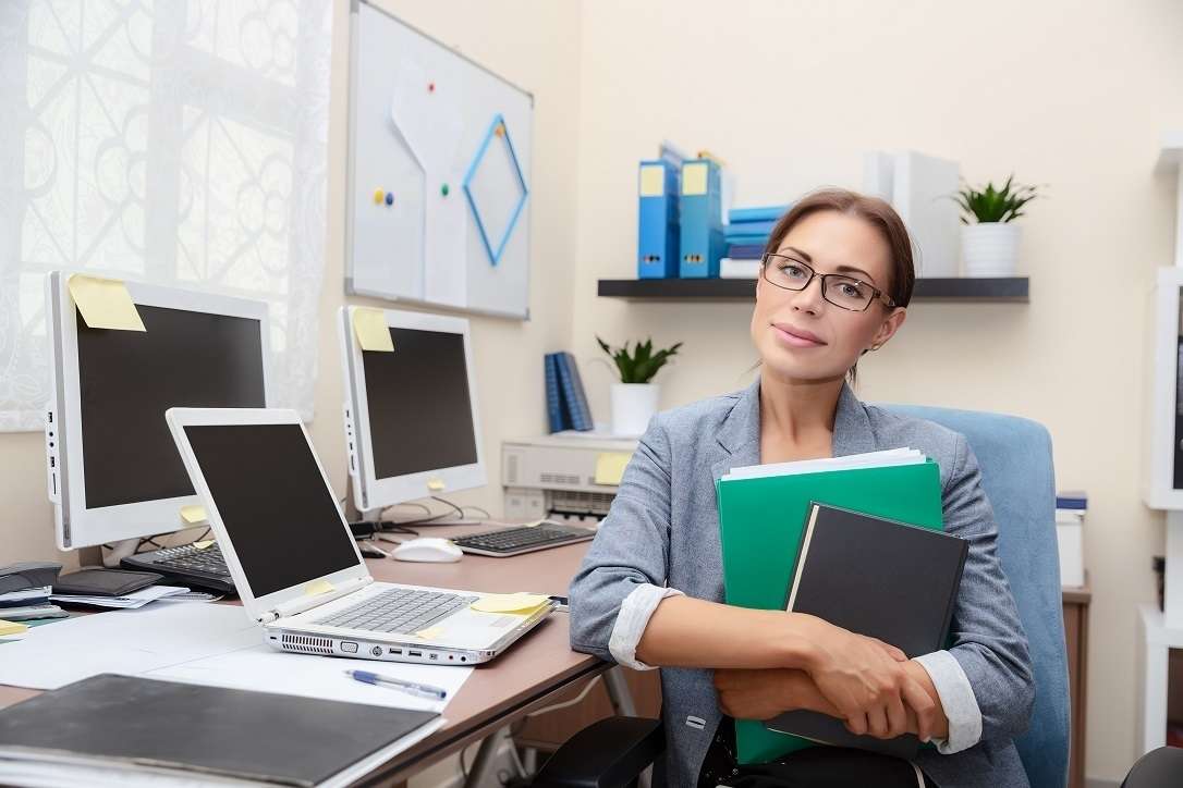 Woman in a work environment with computers in the background.