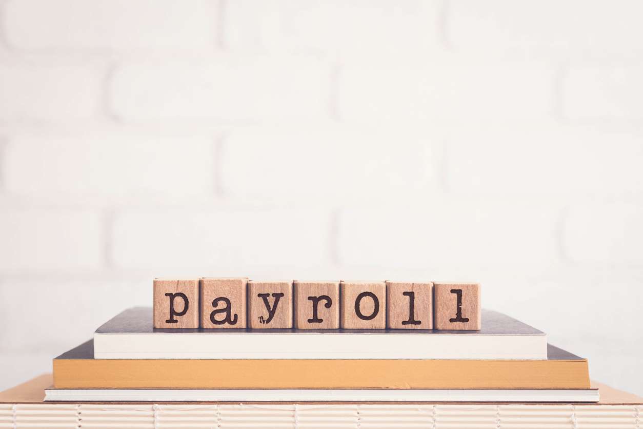 The word "Payroll" spelled on wooden cubes that are placed on the top of books.