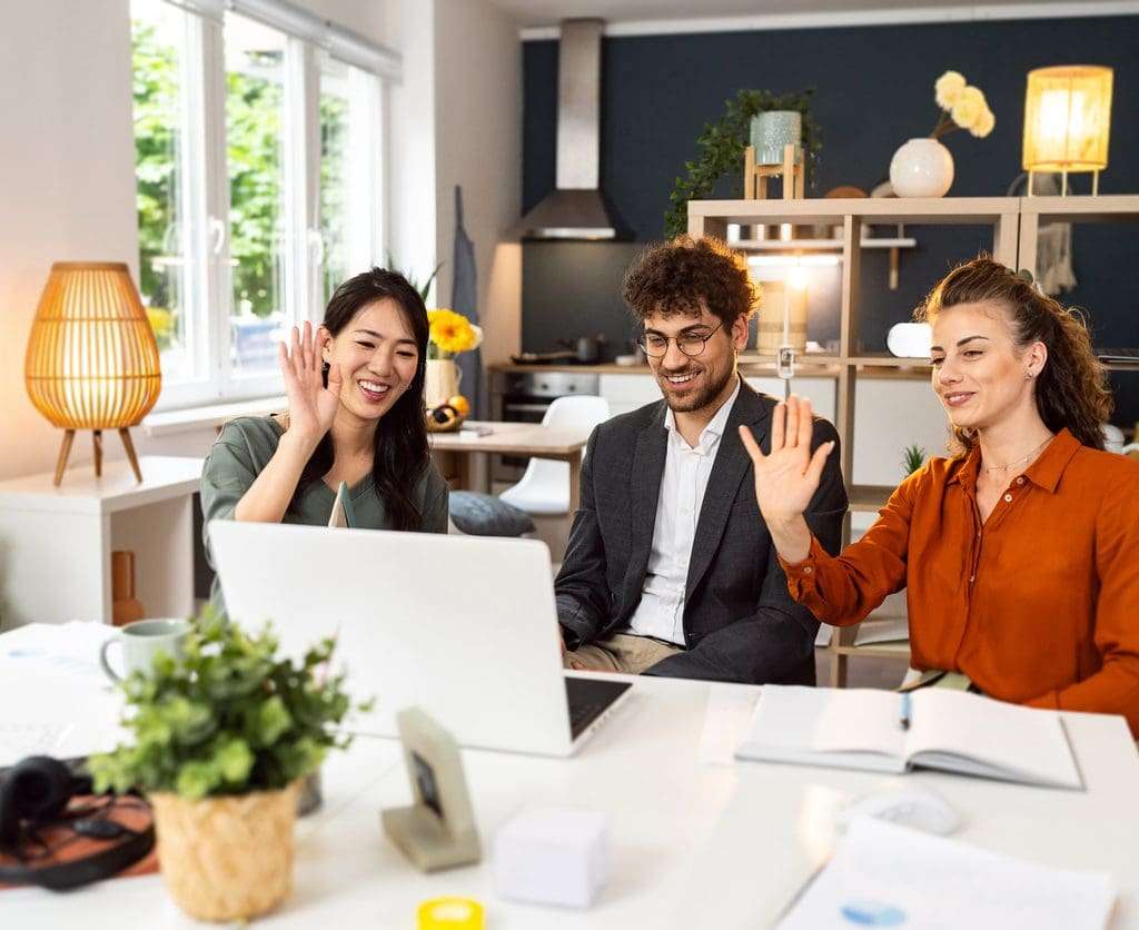 Multiracial female and male coworkers waving during a video call from the office.