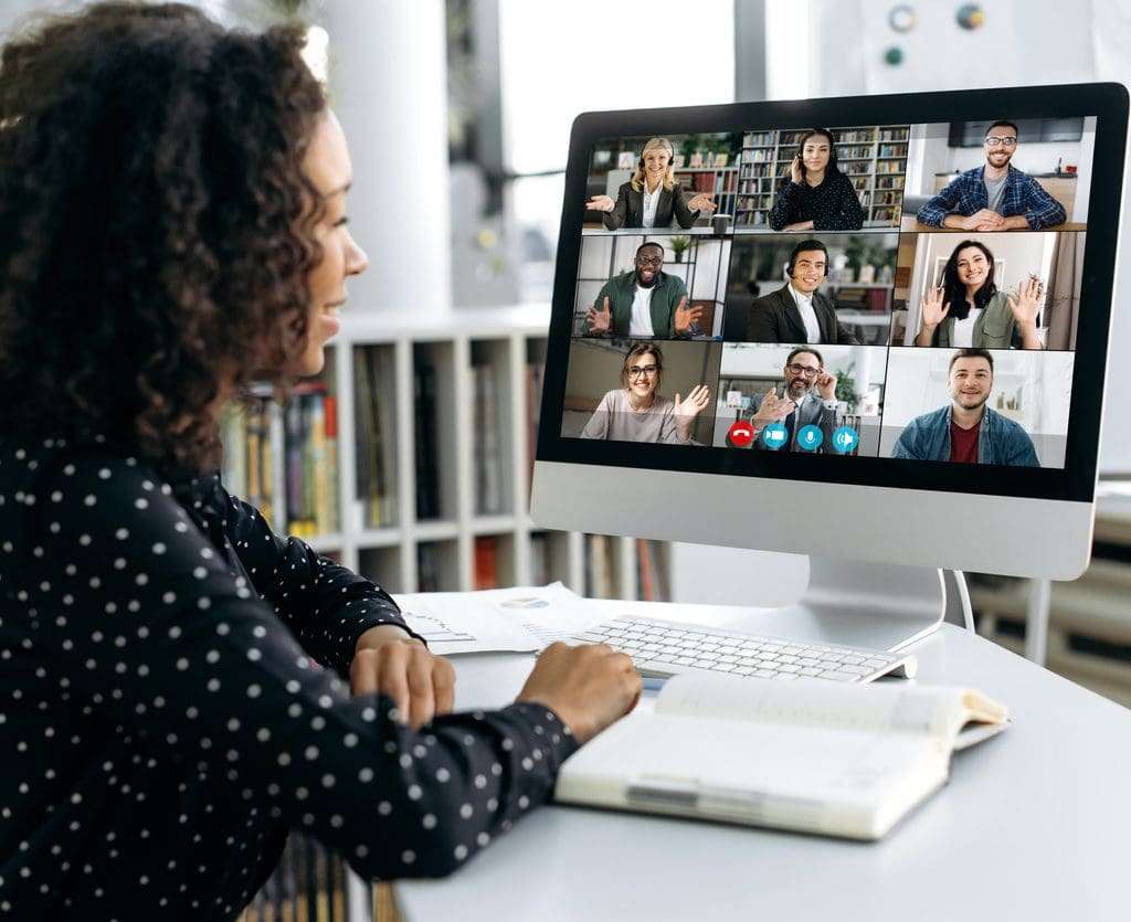 Woman sitting in front of a computer, talking to colleagues online.