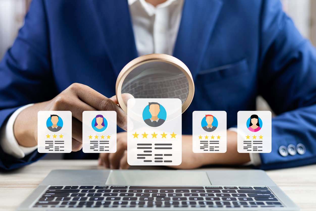 Hiring for hybrid positions - A businessman holding a magnifying glass over potential online employees.