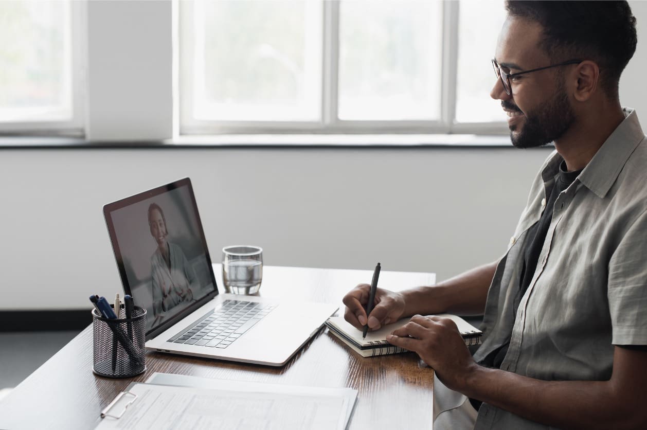 Remote onboarding buddy - A male employee having a virtual meeting with his mentor using a laptop.